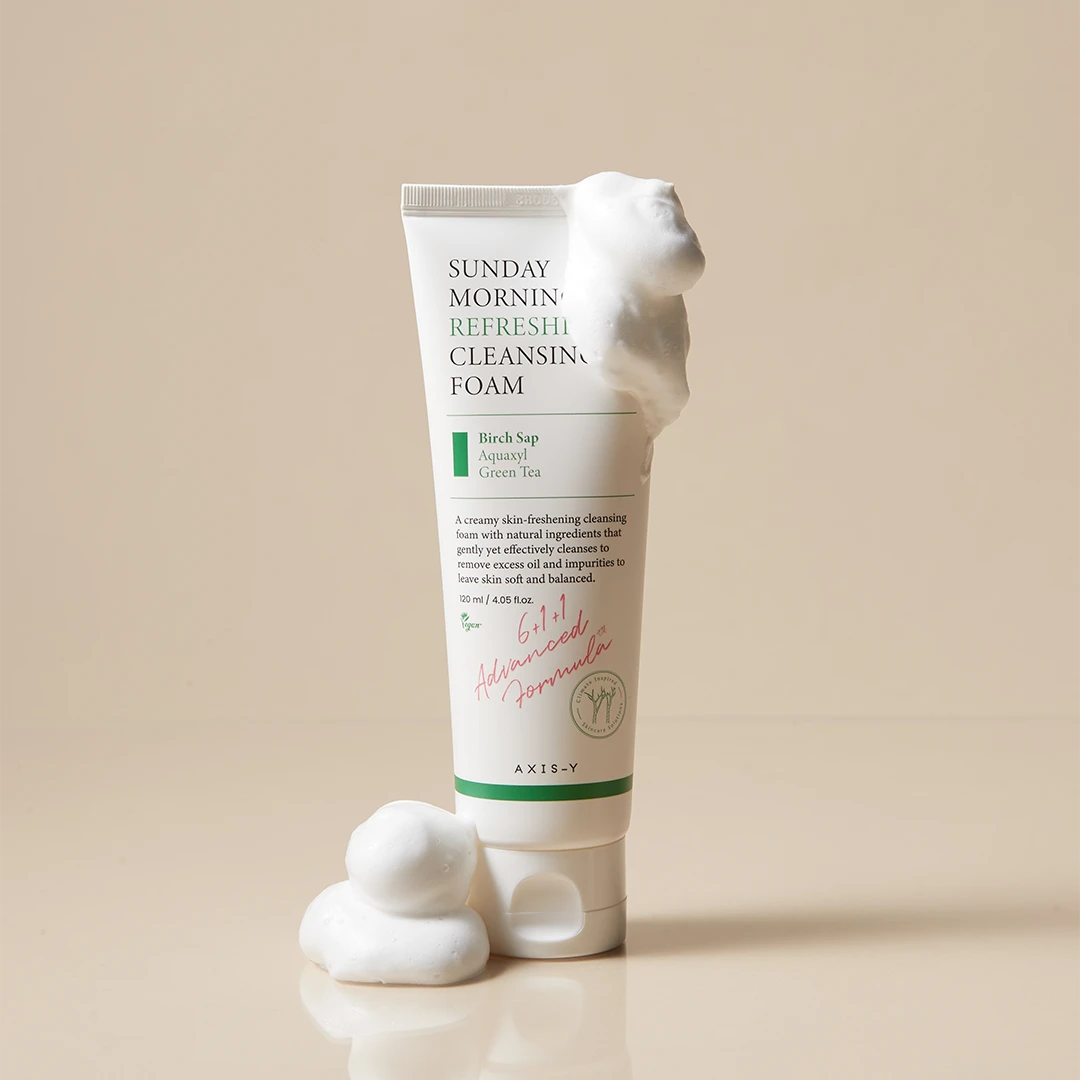 Tube of Sunday Morning Refresh Cleansing Foam with foam on a beige background