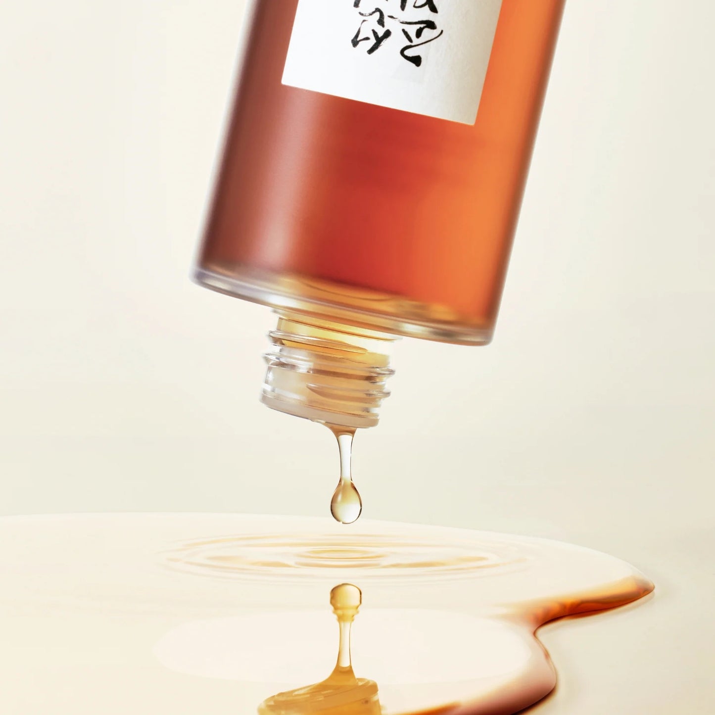 Close-up of a bottle with a droplet of liquid on a beige background