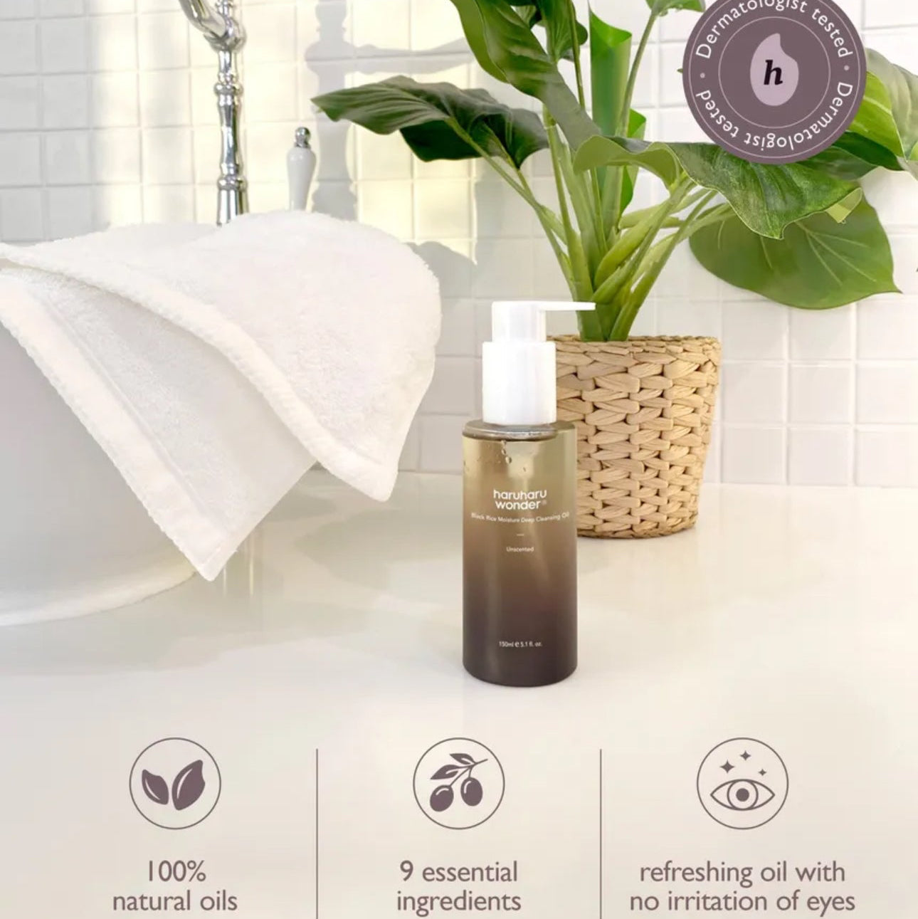 Bottle of hair oil on a bathroom counter with a plant and shower in the background, featuring a 'Vegan' label.