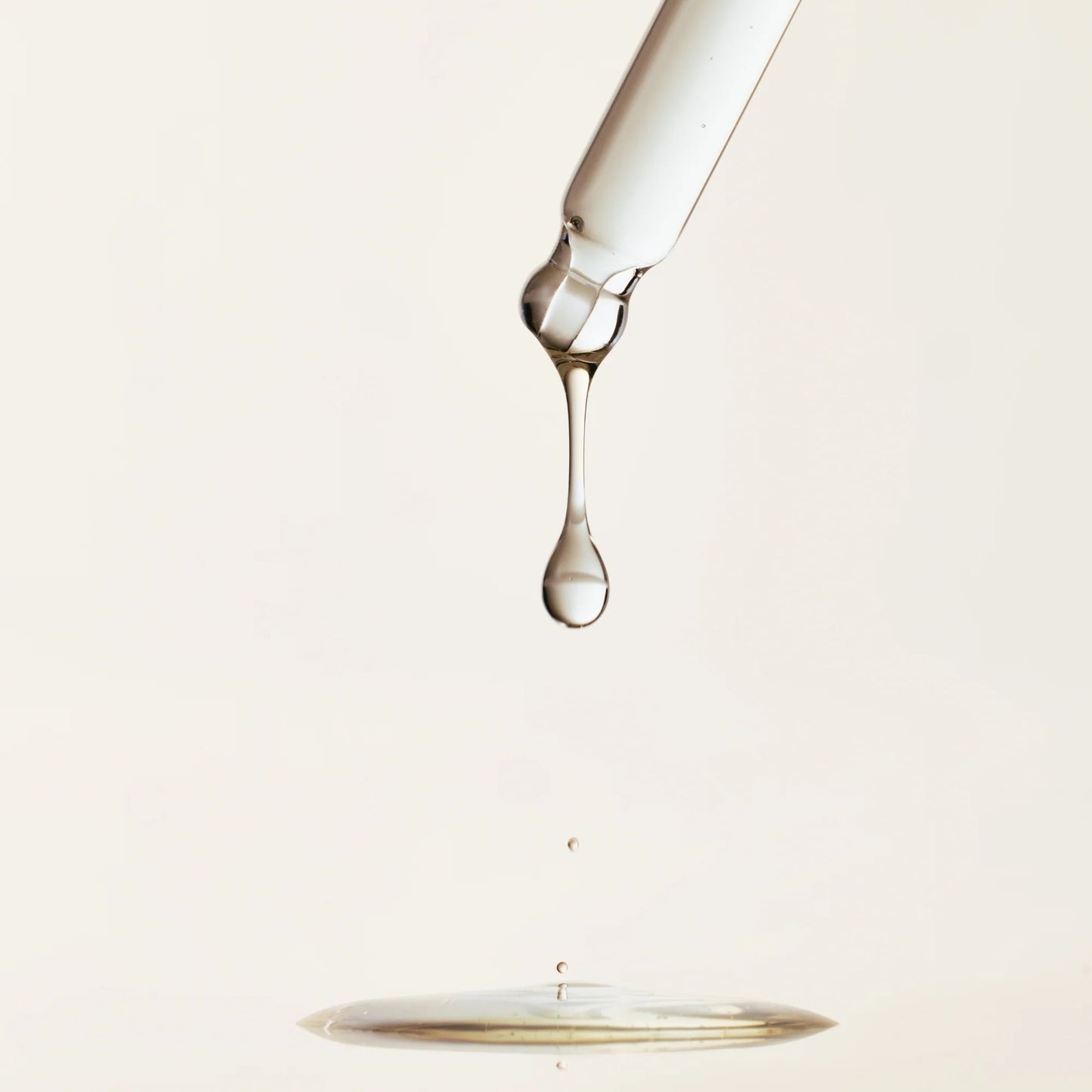 Glass bottle with a droplet of liquid on a light beige background