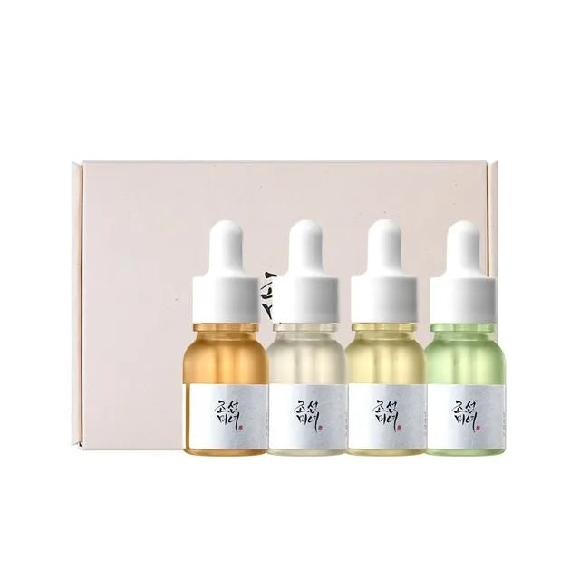 Four dropper bottles with different colored liquids in front of a pink box on a white background