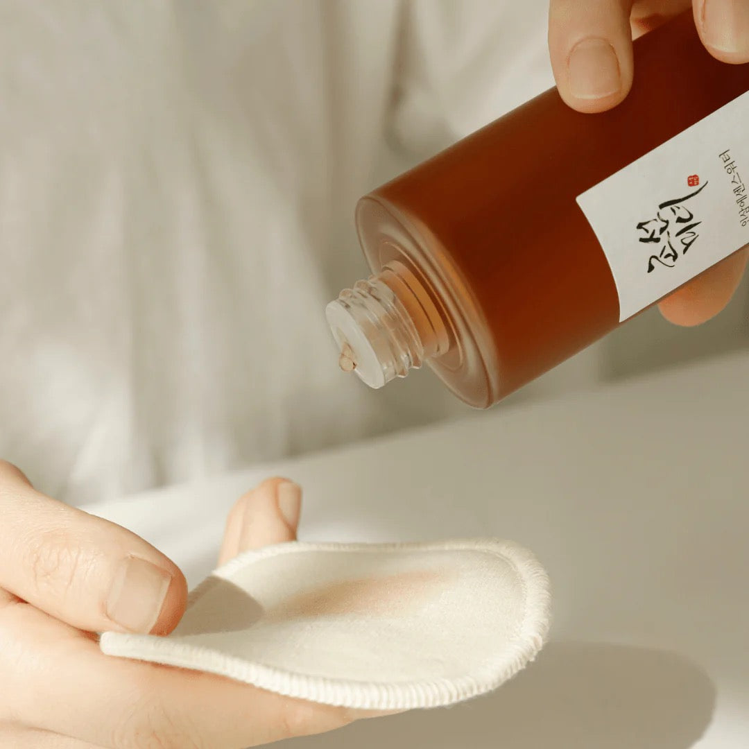 Person pouring liquid from a brown bottle labeled 'Nippon' onto a white cloth against a neutral background.