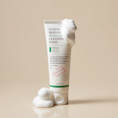 Tube of Sunday Morning Refresh Cleansing Foam with foam on a beige background