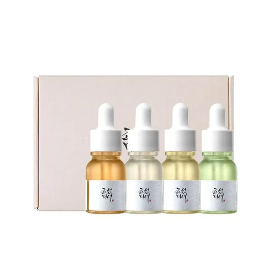 Four dropper bottles with different colored liquids in front of a pink box on a white background